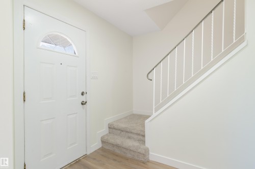 Entryway featuring a white paneled door with an arched glass insert, wood-finish flooring, and a carpeted staircase with a metal railing - 15C Callingwood Crest, Edmonton, AB - Indoor Photo Showing Other Room