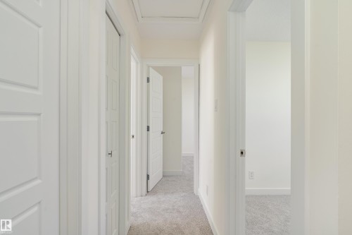 Hallway featuring light-toned carpeting, white walls, and white paneled doors with chrome hardware - 15C Callingwood Crest, Edmonton, AB - Indoor Photo Showing Other Room