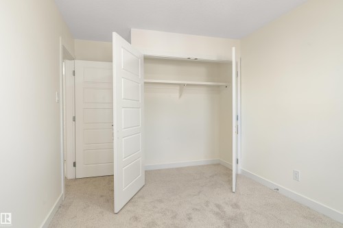 Neutral-toned room featuring a closet with bi-fold paneled doors and built-in shelving, complemented by a solid paneled interior door, light-colored walls, and carpet flooring - 15C Callingwood Crest, Edmonton, AB - Indoor Photo Showing Other Room