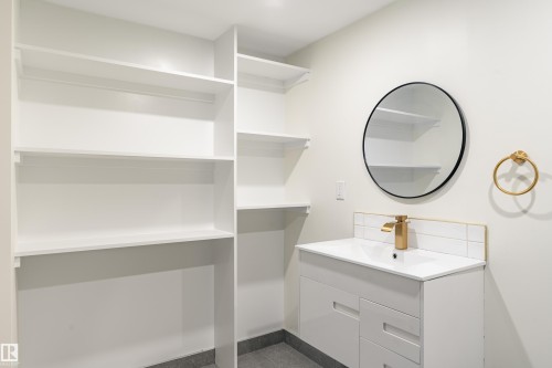 Built-in shelving and vanity with modern gold-tone faucet, round black-framed mirror, and white subway tile backsplash - 15C Callingwood Crest, Edmonton, AB - Indoor