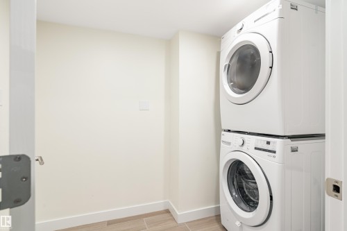 Dedicated laundry area featuring a white stacked washer and dryer, light-toned walls, and wood-finish tile flooring - 15C Callingwood Crest, Edmonton, AB - Indoor Photo Showing Laundry Room