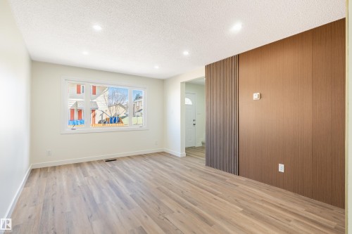 Spacious interior featuring wide-plank wood-finish flooring, a large picture window, recessed lighting, and a distinctive wood-paneled accent wall with vertical slat detailing - 15C Callingwood Crest, Edmonton, AB - Indoor Photo Showing Other Room