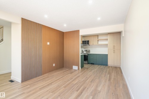 Open-concept living area featuring wood-finish flooring, recessed lighting, and a slatted wood accent wall - 15C Callingwood Crest, Edmonton, AB - Indoor