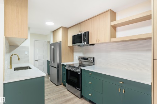 Modern kitchen featuring two-tone cabinetry, stainless steel appliances, white countertops, a tiled backsplash, and wood-finish flooring - 15C Callingwood Crest, Edmonton, AB - Indoor Photo Showing Kitchen