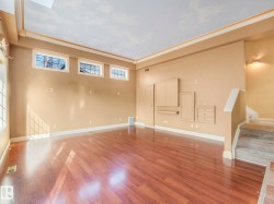 Spacious room featuring rich wood-finish flooring, high ceilings with crown molding, and multiple windows - 
