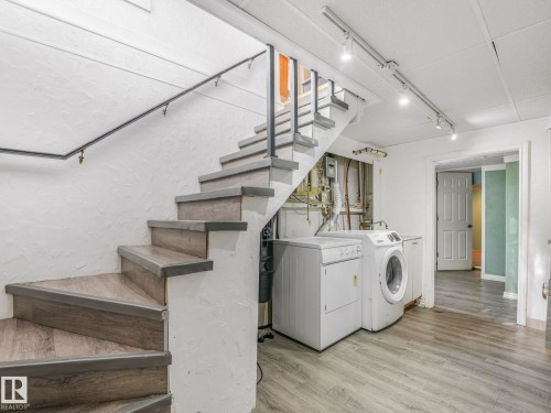 Wood-finish flooring throughout, featuring a spiral staircase with dark handrail, track lighting, and a dedicated laundry area - 11643 76 Avenue, Edmonton, AB - Indoor Photo Showing Laundry Room