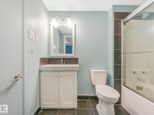 Bathroom featuring a single vanity with storage, a rectangular mirror, and a combination shower/bathtub with a sliding glass enclosure - 11643 76 Avenue, Edmonton, AB - Indoor Photo Showing Bathroom