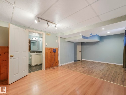 Spacious room featuring light wood-finish flooring transitioning to darker wood-finish flooring, a drop ceiling with track lighting and recessed lighting, and a partial wood paneled wall - 11643 76 Avenue, Edmonton, AB - Indoor