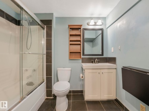 Bathroom featuring a full-size tub with sliding glass doors, a single vanity with storage, and dark tile flooring - 11643 76 Avenue, Edmonton, AB - Indoor Photo Showing Bathroom