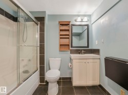 Bathroom featuring a full-size tub with sliding glass doors, a single vanity with storage, and dark tile flooring - 