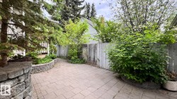 Paved patio featuring a segmented retaining wall, mature perimeter foliage, and a wood fence - 