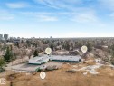Expansive property featuring a large building with a white facade and green trim, a paved parking area, fenced outdoor spaces, a natural grass field, and mature surrounding trees - 11643 76 Avenue, Edmonton, AB  - Outdoor With View 