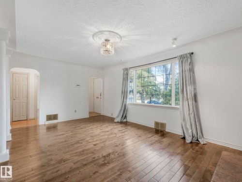 Spacious room featuring wood-finish flooring, a large multi-pane window, and a decorative ceiling light fixture - 11643 76 Avenue, Edmonton, AB - Indoor Photo Showing Other Room