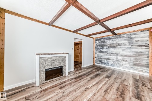 Living area featuring wood-finish flooring, a decorative stone-clad fireplace with a light-colored mantel, and exposed wood beam ceiling details - 3325 107 Avenue Nw, Edmonton, AB - Indoor With Fireplace