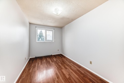 Room featuring a window with exterior tree scenery, wood-finish flooring, light gray walls, and a textured ceiling with a flush-mount light fixture - 3325 107 Avenue Nw, Edmonton, AB - Indoor Photo Showing Other Room