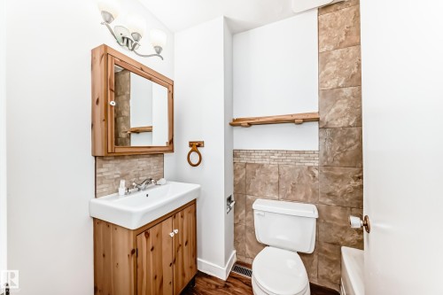 Bathroom featuring a wall-mounted vanity with integrated sink, wood-finish cabinetry, coordinating medicine cabinet, and a tiled accent wall - 3325 107 Avenue Nw, Edmonton, AB - Indoor Photo Showing Bathroom