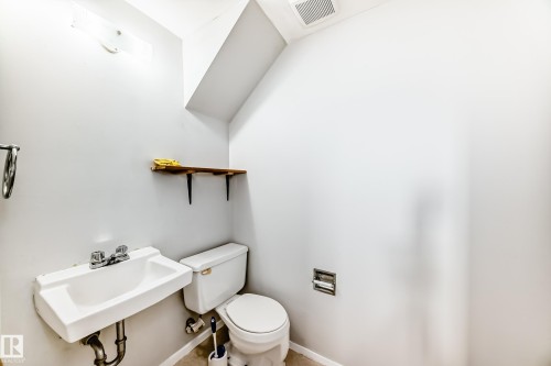 Compact bathroom featuring a wall-mounted sink, a toilet, a wooden wall shelf, and light gray walls - 3325 107 Avenue Nw, Edmonton, AB - Indoor Photo Showing Bathroom