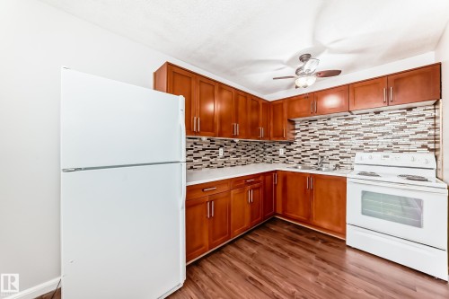 Kitchen featuring wood-finish flooring, wood cabinetry with brushed nickel hardware, white countertops, and a tiled backsplash - 3325 107 Avenue Nw, Edmonton, AB - Indoor Photo Showing Kitchen