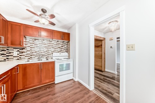 Kitchen featuring wood-finish cabinetry, light-toned countertops, a mosaic tile backsplash, and a white electric range - 3325 107 Avenue Nw, Edmonton, AB - Indoor Photo Showing Kitchen