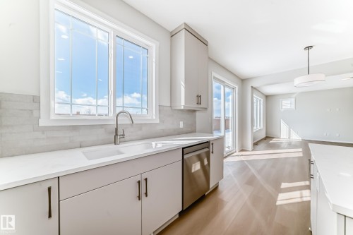 The kitchen features light-colored cabinetry with dark hardware, a stainless steel dishwasher, and a window above the sink - 1516 206 Street Nw, Edmonton, AB - Indoor Photo Showing Kitchen
