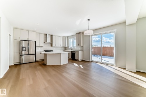 This open-concept area features hardwood floors, a kitchen with stainless steel appliances, light-colored cabinetry, and a central island - 1516 206 Street Nw, Edmonton, AB - Indoor Photo Showing Kitchen With Upgraded Kitchen