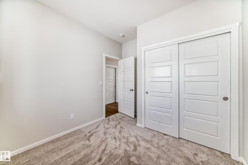 This room features neutral colored walls, light-toned carpet, and white sliding closet doors with horizontal paneling - 1516 206 Street Nw, Edmonton, AB - Indoor Photo Showing Other Room