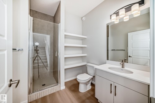 The bathroom features a modern vanity with a white countertop and an undermount sink, a shower with a glass enclosure, and white floating shelves for storage - 1516 206 Street Nw, Edmonton, AB - Indoor Photo Showing Bathroom
