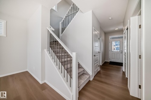The property features a welcoming entryway with hardwood flooring and a carpeted staircase with white risers and dark balusters - 1516 206 Street Nw, Edmonton, AB - Indoor Photo Showing Other Room