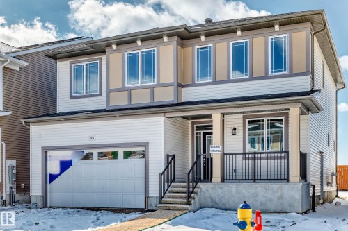 The property features a two-story facade with a neutral color palette, an integrated garage, and a welcoming front porch with dark railings - 1516 206 Street Nw, Edmonton, AB - Outdoor With Facade