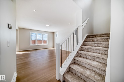 The property features an entryway with light wood flooring, a staircase with carpeting and modern metal balusters, and a spacious area with large windows providing natural light - 1516 206 Street Nw, Edmonton, AB - Indoor Photo Showing Other Room