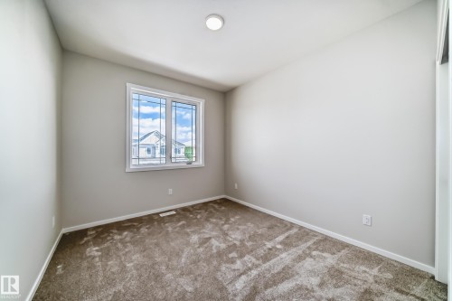 This room features light-colored walls, patterned carpet flooring, and a window with white trim - 1516 206 Street Nw, Edmonton, AB - Indoor Photo Showing Other Room
