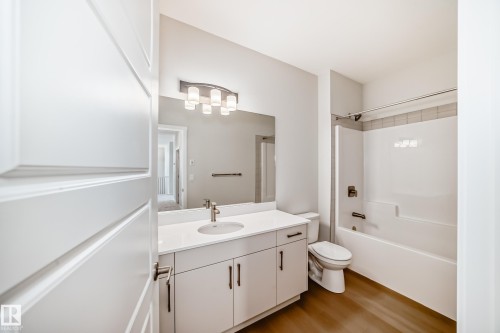 The bathroom features a modern vanity with a white countertop and a single sink, a toilet, and a bathtub with a shower - 1516 206 Street Nw, Edmonton, AB - Indoor Photo Showing Bathroom