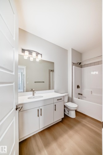 Bathroom featuring a white vanity with a single sink, a large mirror, a toilet, and a bathtub with a shower - 1516 206 Street Nw, Edmonton, AB - Indoor Photo Showing Bathroom