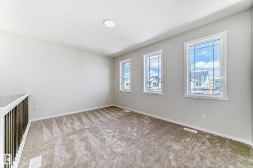 This bright room features three large windows that allow for ample natural light, a neutral color palette, and carpeted flooring - 1516 206 Street Nw, Edmonton, AB - Indoor Photo Showing Other Room