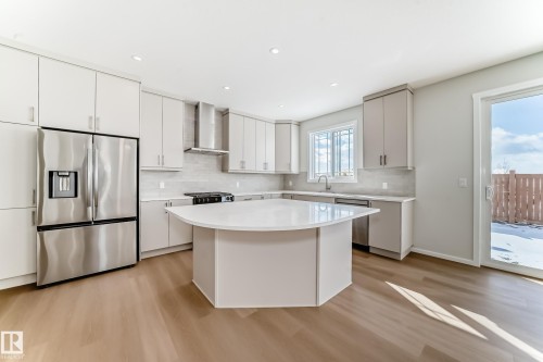 The property features a bright kitchen with light wood flooring, an island with a white countertop, and stainless steel appliances - 1516 206 Street Nw, Edmonton, AB - Indoor Photo Showing Kitchen With Upgraded Kitchen