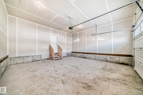 Spacious garage featuring a concrete floor, an overhead door, and a utility door with wooden steps - 1516 206 Street Nw, Edmonton, AB - Indoor Photo Showing Garage
