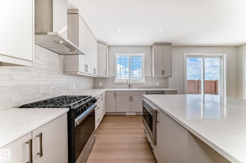 Modern kitchen featuring light cabinetry, a gas range with a stainless steel hood, light countertops, and a sliding glass door - 1516 206 Street Nw, Edmonton, AB - Indoor Photo Showing Kitchen With Upgraded Kitchen