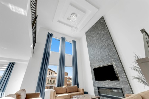 Two-story living area featuring a stacked stone fireplace with an integrated media center, soaring windows, and a coffered ceiling with a tiered light fixture - 1923 19 Avenue, Edmonton, AB - Indoor Photo Showing Other Room With Fireplace