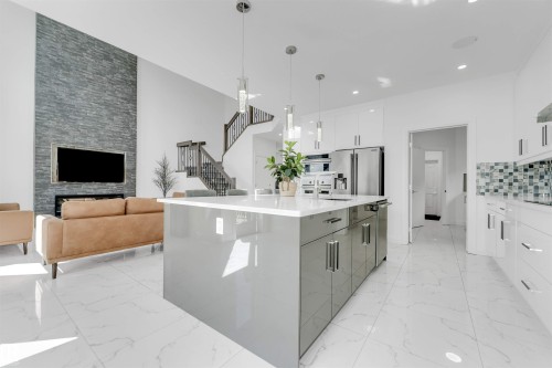 Open-concept living space featuring a gourmet kitchen island, high ceilings, a full-height stone fireplace, a modern staircase, and white tile flooring - 1923 19 Avenue, Edmonton, AB - Indoor Photo Showing Kitchen With Upgraded Kitchen
