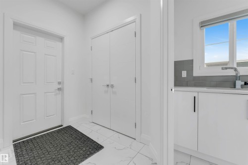 Entry foyer featuring panel-style entry door, double-door closet, and white marble-look tile flooring - 1923 19 Avenue, Edmonton, AB - Indoor Photo Showing Other Room