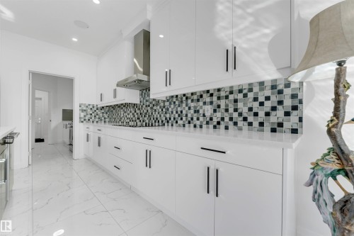 Sleek kitchen featuring white cabinetry with black hardware, white countertops, and a patterned tile backsplash - 1923 19 Avenue, Edmonton, AB - Indoor Photo Showing Kitchen