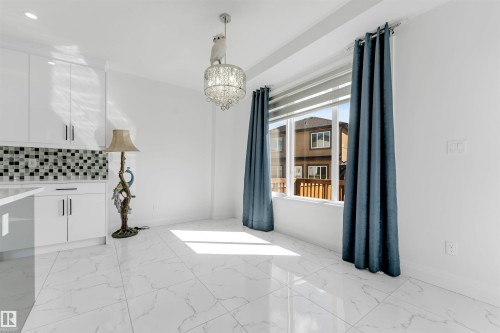 Bright interior space featuring white tile flooring, a large window with roller shades, and a decorative chandelier - 1923 19 Avenue, Edmonton, AB - Indoor
