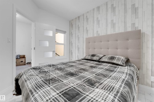 Bedroom featuring a padded tufted headboard, wood-finish accent wall, and a modern interior door with frosted glass panels - 1923 19 Avenue, Edmonton, AB - Indoor Photo Showing Bedroom