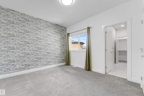 Bedroom featuring a striking gray brick-patterned accent wall, light gray carpeting, and a window with a green drape - 1923 19 Avenue, Edmonton, AB - Indoor Photo Showing Other Room