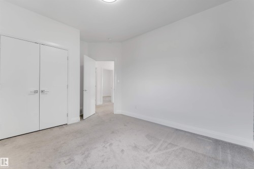 Carpeted room featuring a double-door closet with modern hardware, white trim, and light-colored walls - 1923 19 Avenue, Edmonton, AB - Indoor Photo Showing Other Room