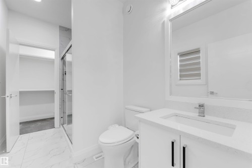 Bathroom featuring a white vanity with integrated sink and chrome faucet, a frameless mirrored medicine cabinet, a toilet, a glass-enclosed shower, and white tile flooring - 1923 19 Avenue, Edmonton, AB - Indoor Photo Showing Bathroom