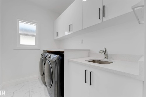 Utility room featuring white cabinetry with dark pulls, white countertop with an undermount sink and chrome faucet, and a window with frosted glass - 1923 19 Avenue, Edmonton, AB - Indoor Photo Showing Laundry Room