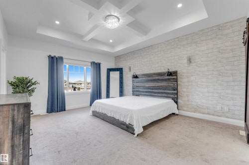 Spacious room featuring a tray ceiling with a central chandelier, recessed lighting, and an accent wall with stacked stone-look detailing - 1923 19 Avenue, Edmonton, AB - Indoor Photo Showing Bedroom