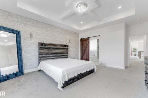 Spacious sleeping area featuring a tray ceiling with a chandelier, light grey carpeting, and a textured accent wall - 1923 19 Avenue, Edmonton, AB - Indoor Photo Showing Bedroom