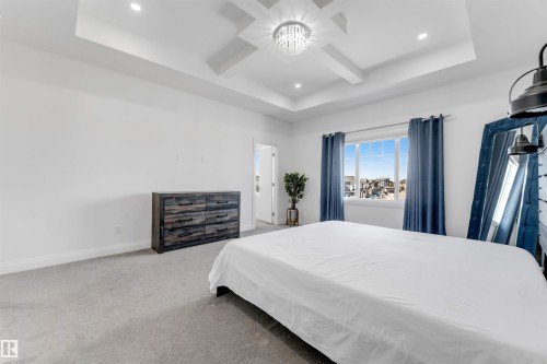 Spacious room featuring a tray ceiling with a central chandelier and recessed lighting, large window with blue privacy drapes, and gray carpeting - 1923 19 Avenue, Edmonton, AB - Indoor Photo Showing Bedroom